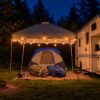 Nighttime canopy string light setup beside an RV, with an edited campfire lifestyle scene. Hooks only; lights, canopy and camping items not included.